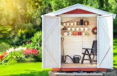 Small white garden shed with doors open and garden background.