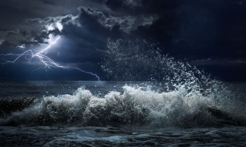 Angry waves with bolts of lightening from a storm at night.