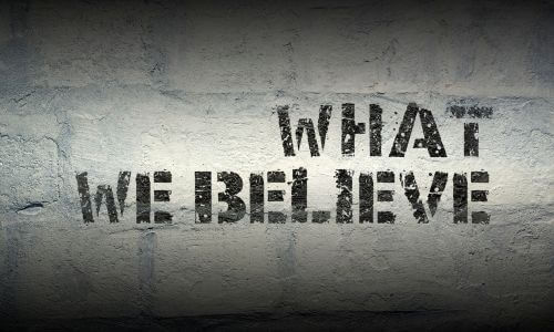 Sign with "What We Believe" in black letters on white painted brick wall.