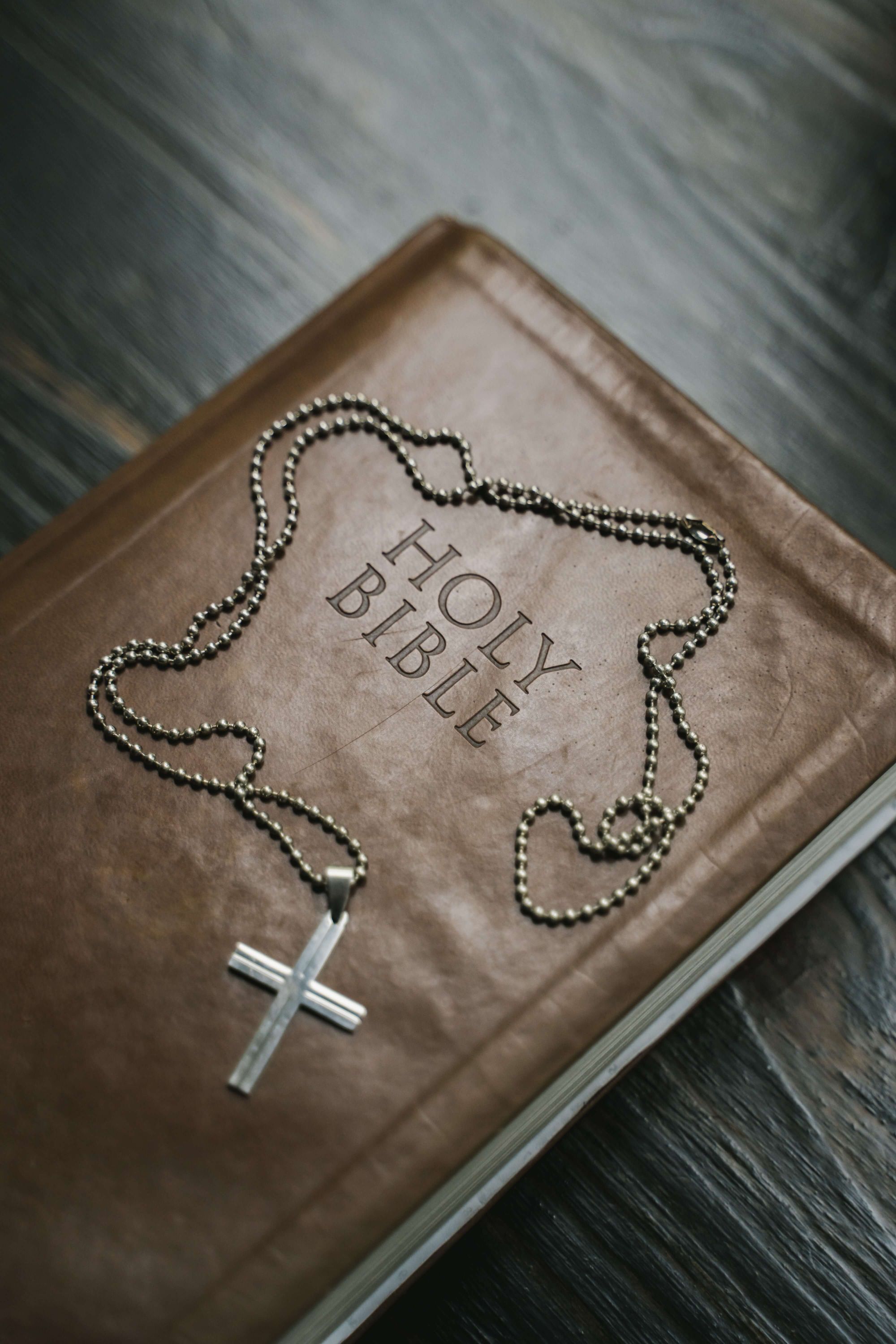 Holy Bible with a silver cross on a chain laying on top