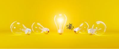 Bright light bulb in the center of a yellow wall with other bulbs lying around it.