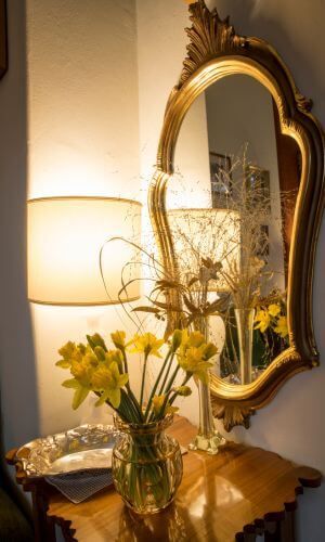 Antique, gold-framed mirror over a side table with vase of daffodils