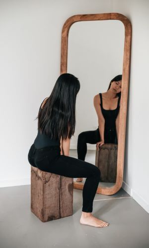 Dancer dressed in black leotards sitting on box in front of rectangular, wood-framed floor mirror